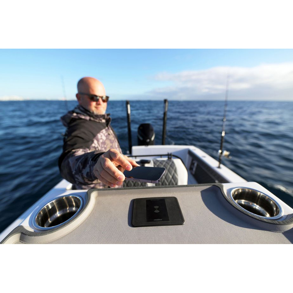 Man on boat holding a smartphone at sea.