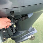 Hand attaching hose to outboard motor water inlet.