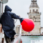 Person holding red buoy on boat near tower.