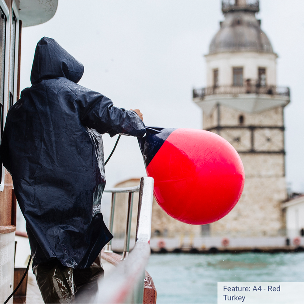 Person handling buoy near lighthouse in raincoat.