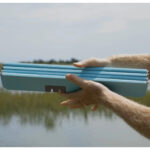 Person holding blue folding chair outdoors.